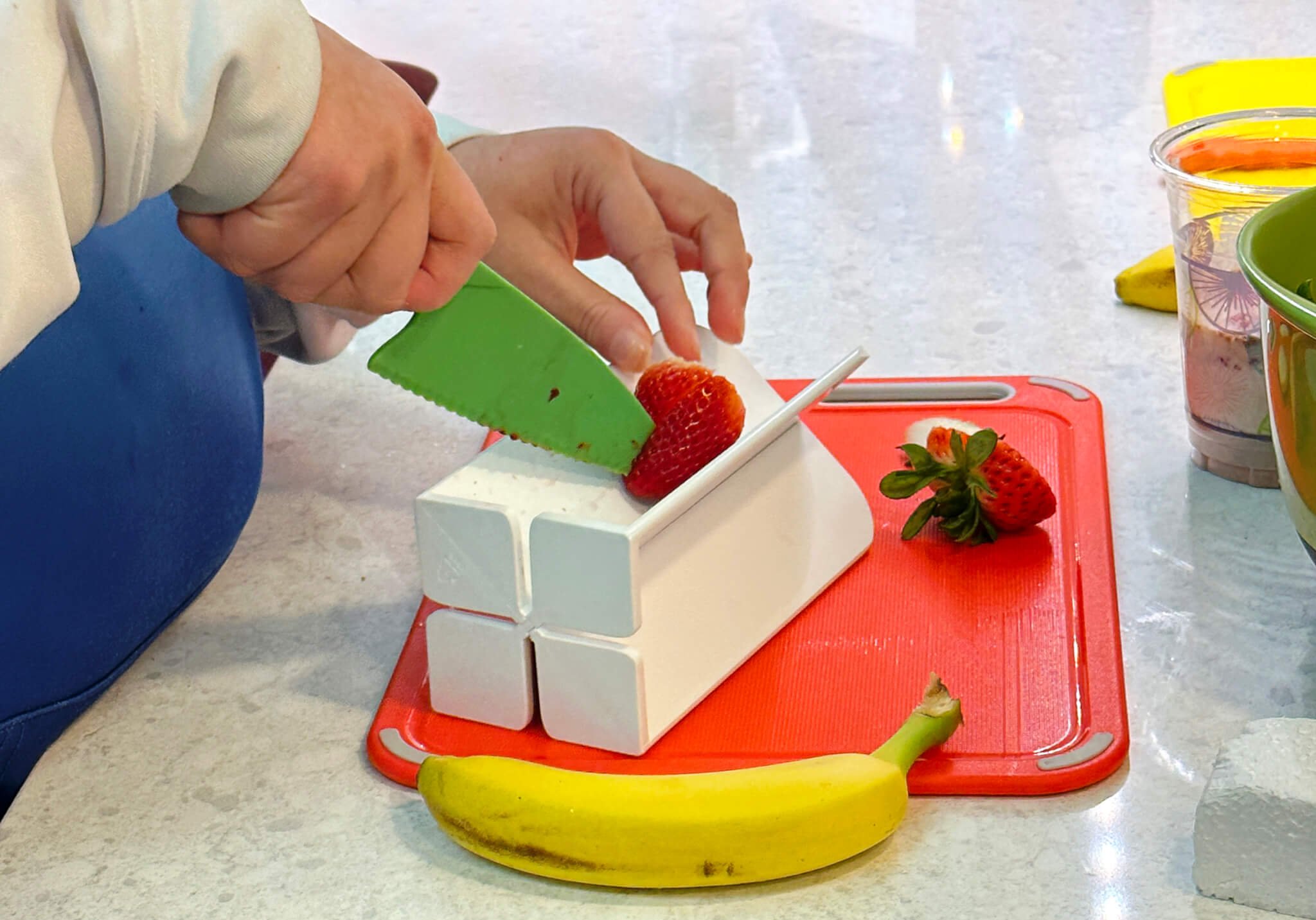 knife slicing a strawberry on a cutting board modified with assistive technology to stabilize the fruit