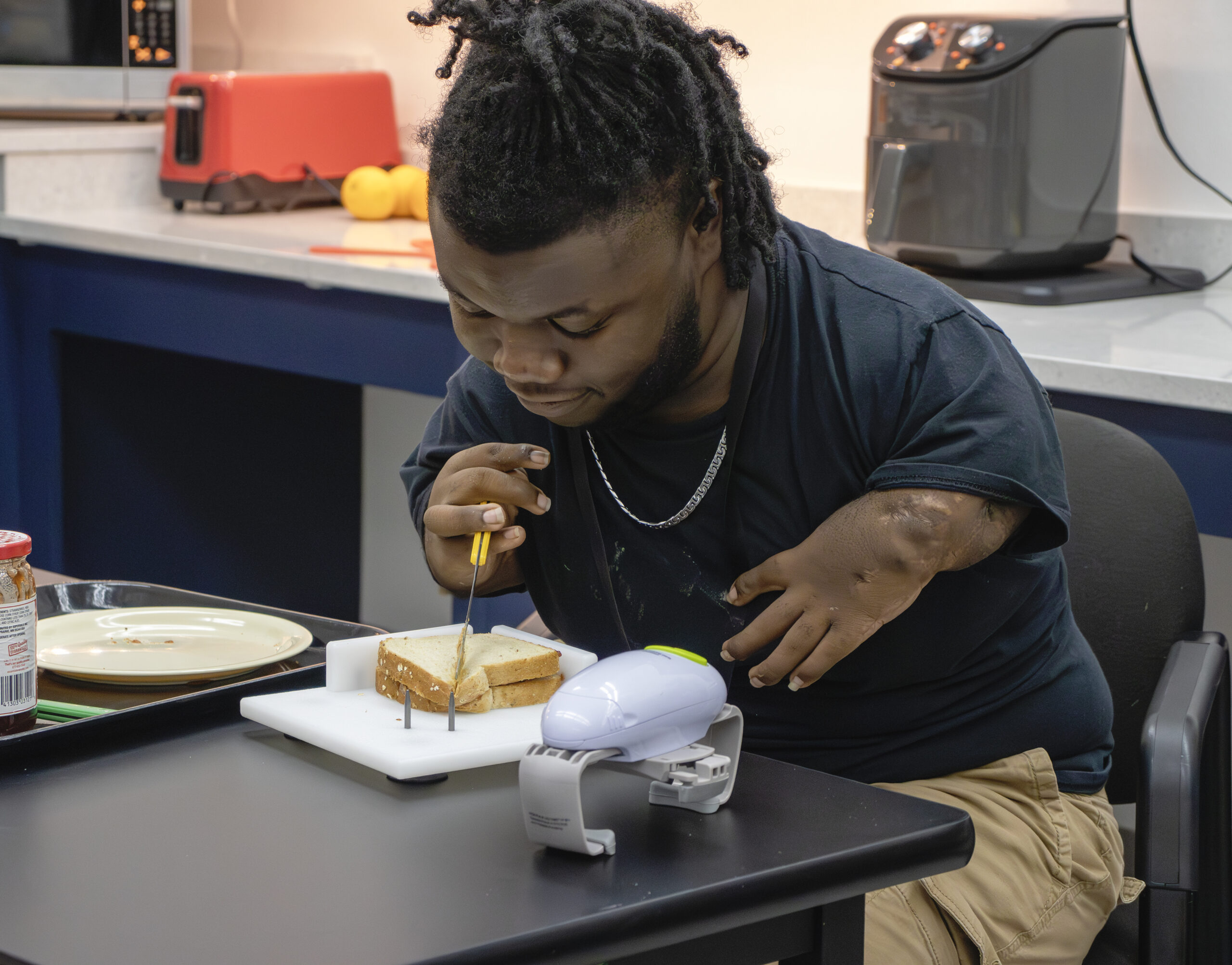 IATP Customer Using an Adaptive Cutting Board to Slice a Sandwich IATP Customer Using an Adaptive Cutting Board to Slice a Sandwich